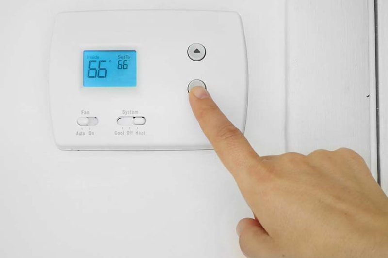 white thermostat with hand adjusting buttons