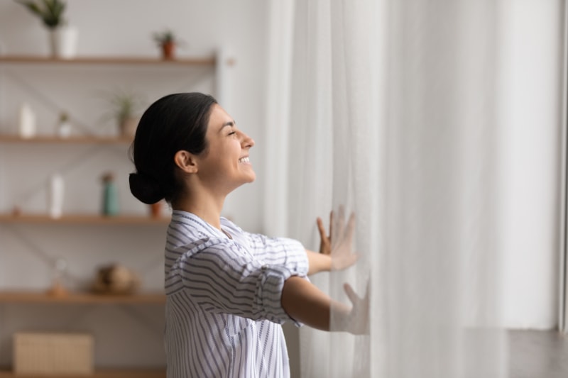 Why Ductless is the Way to Go - Bathing in sunlight. Excited young indian lady meet first morning at new flat house part curtains enjoy being homeowner. Happy hindu female open drapes on window breath fresh air close eyes in delight
